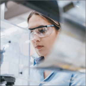 A woman wearing safety goggles works on a machine