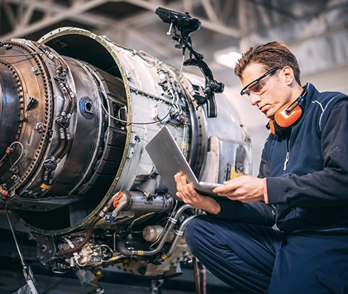 A man wearing safety goggles works on an electrical component of an airplane.