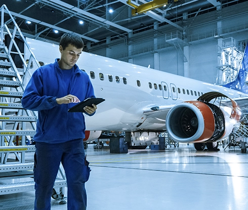 A man stands in an airplane hanger looking at a tablet.