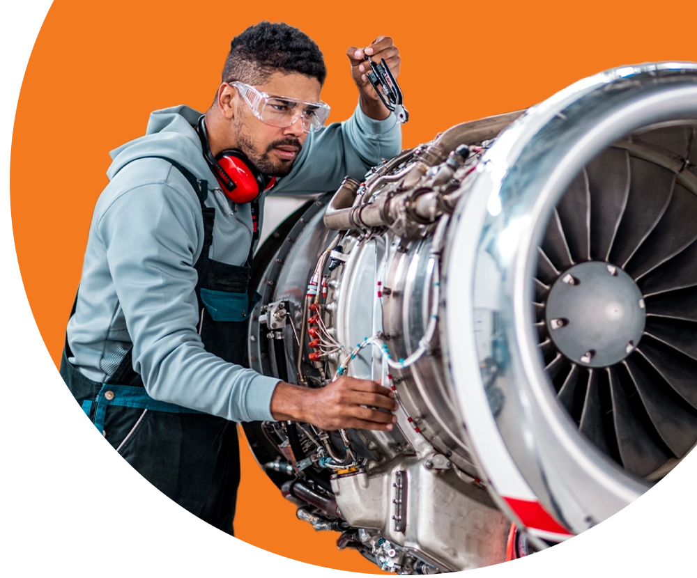 A man wearing safety goggles works on a plane turbine.