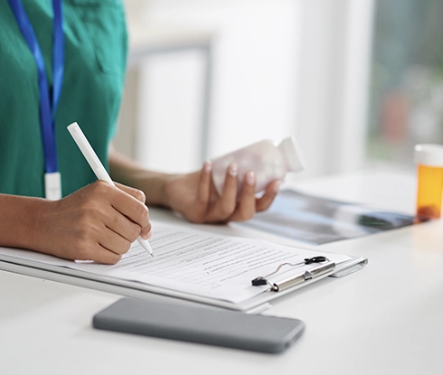 A healthcare professsional writes prescription notes on a document attached to a clipboard.