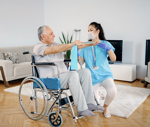 A medical professional helps an elderly patient in a wheelchair do resistance band exercises.