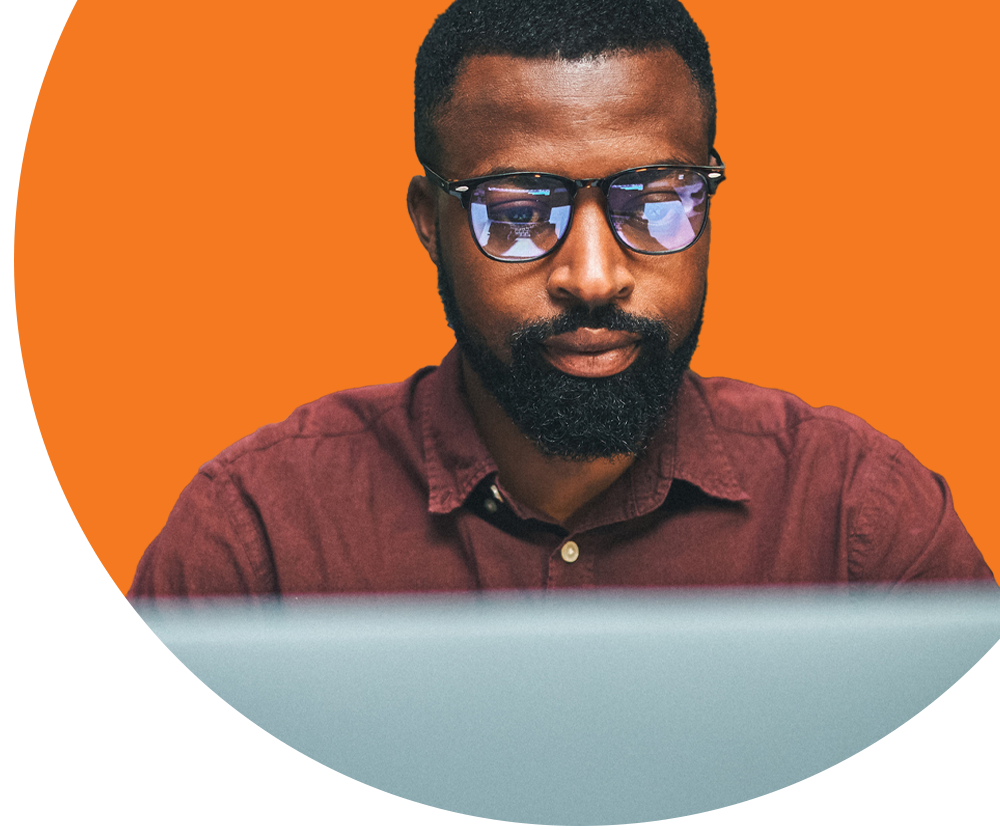 A man wearing glasses looks down at a laptop.