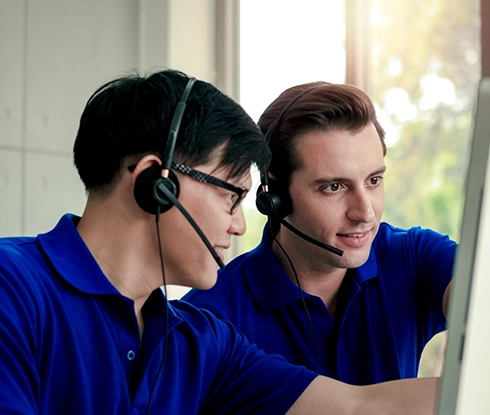 Two men wearing headsets look at a computer monitor